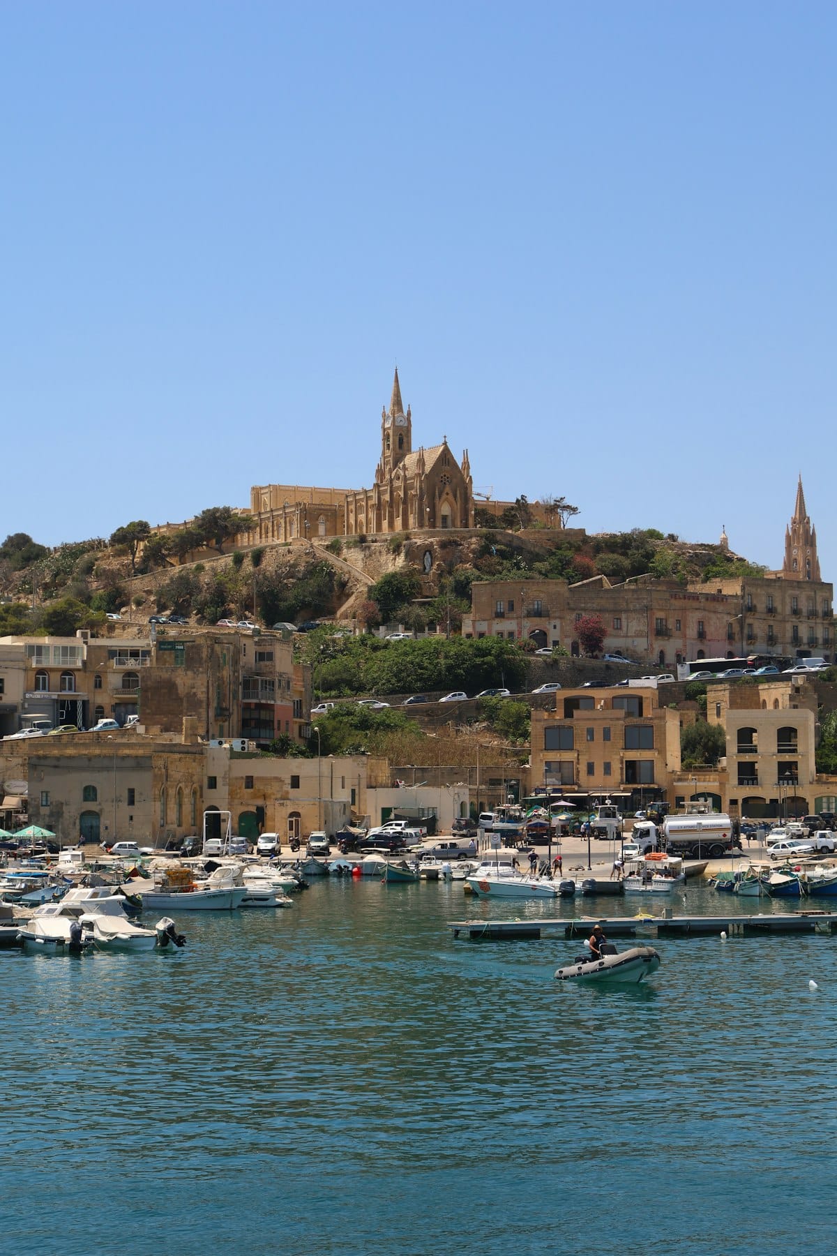 Mġarr Harbour with boats and Lourdes Chapel on the hill in Gozo, Malta